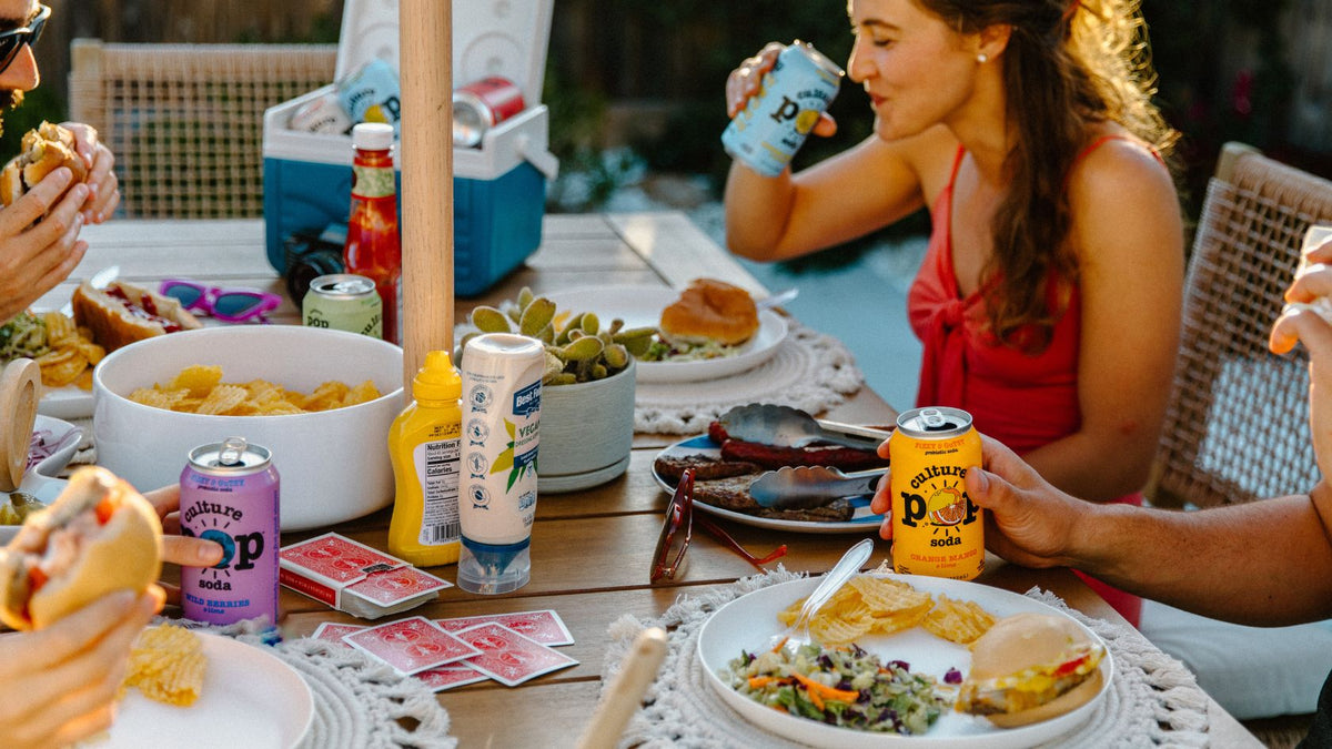 a group of people at a dinner table enjoying food and drinking a can of culture pop